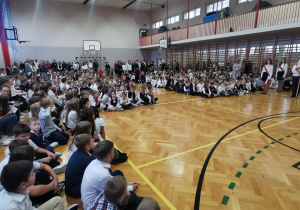 Na zdjeciu widać społeczność szkolną, która zebrała się na apelu w sali gimnastycznej.