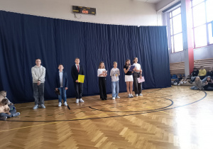 Kandydaci podczas prezentowania swoich programów wyborczych. Stoją uśmiechnięci w sali gimnastycznej.