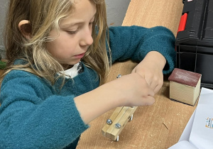 Na fotografii widać uczennicę, wykonującą reniferka z drewna.