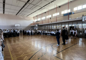 Na zdjęciu widać społeczność szkolną, zebraną w sali gimnastycznej.