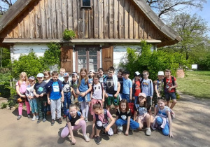 Na zdjęciu widać uczniów. W tle znajduje się jeden z budynków skansenu w Ogrodzie Botanicznym.