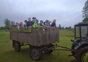 Na fotografii widać uczniów, którzy znajdują się w przyczepie ciągniętej przez traktor.