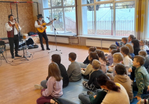 Na fotografii widać trio - panów grających na instrumentach oraz publiczność oglądającą występ.